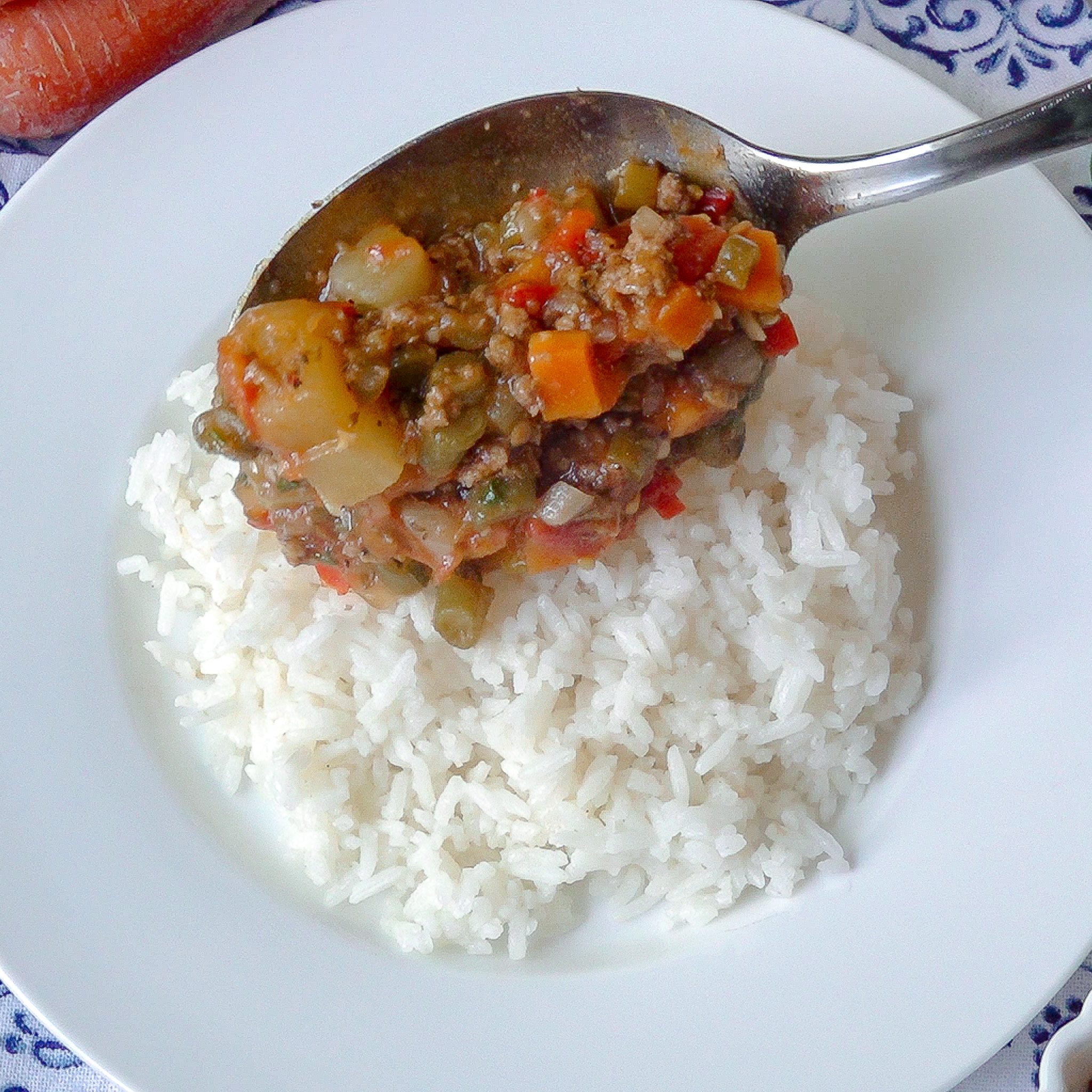 Plato blanco redondo con arroz blanco por encima, una cuchara con picadillo que se coloca sobre el arroz cocinado.