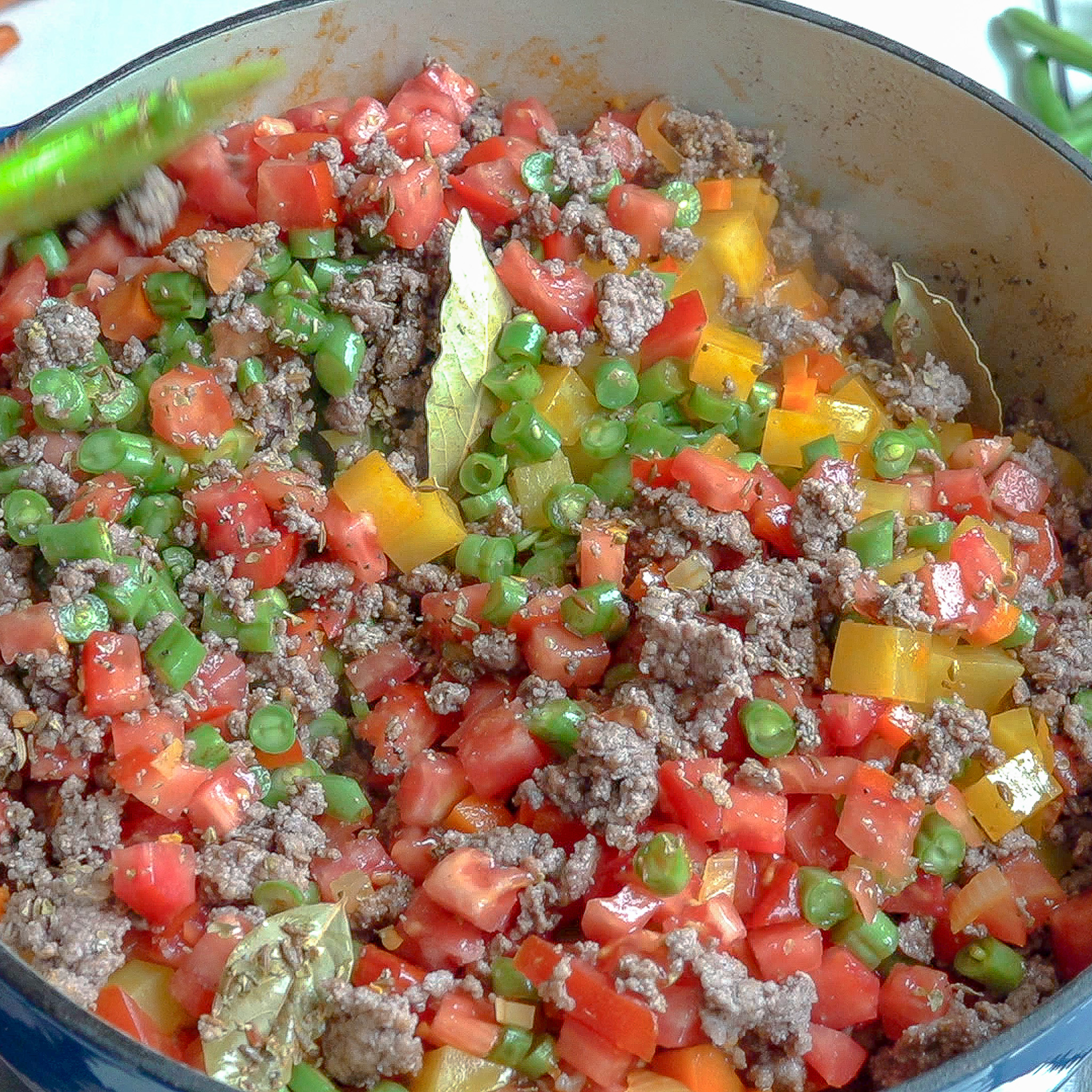 Olla grande con todos los ingredientes crudos, estan revueltos y sobresale una hoja de laurel