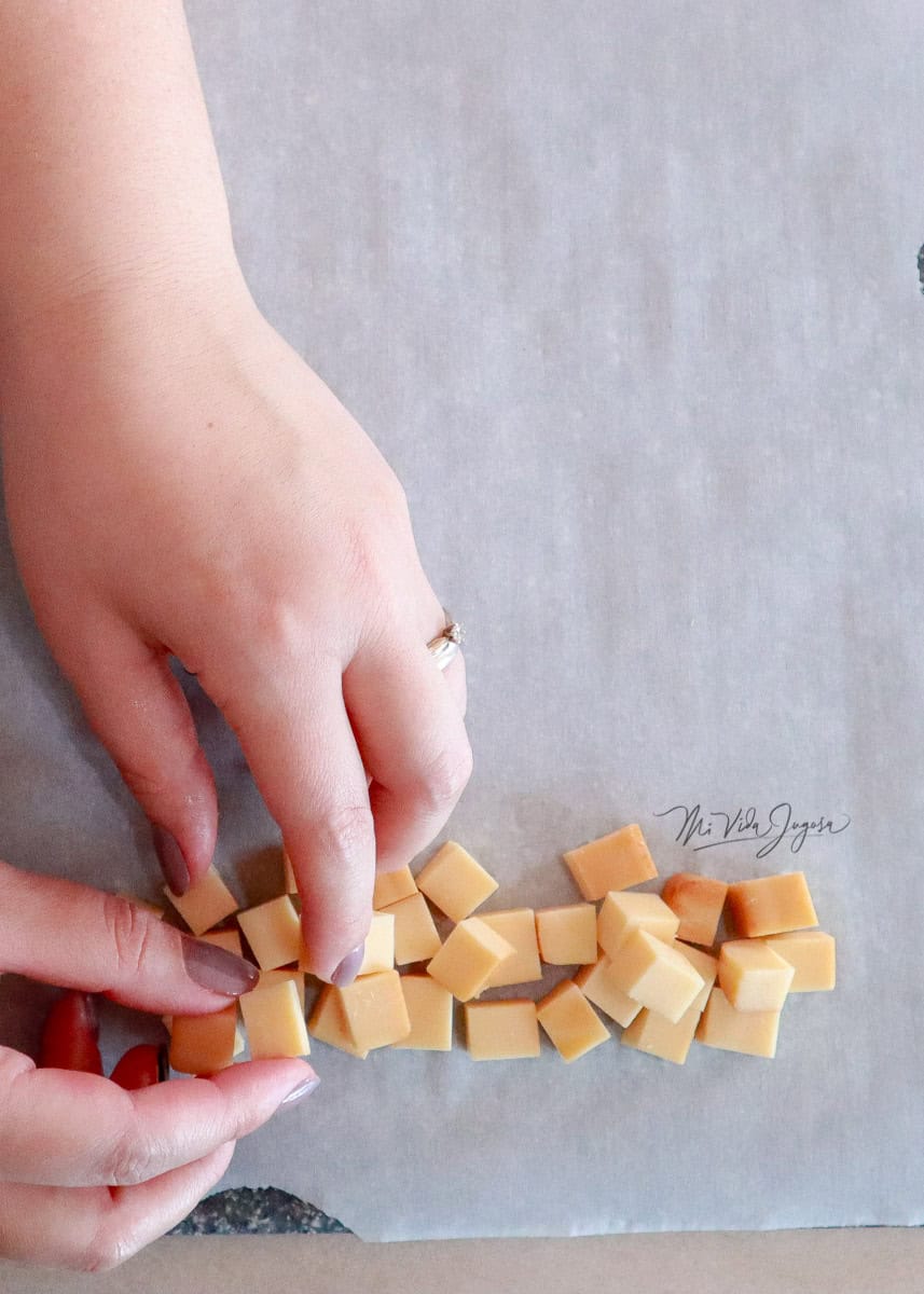 Cubos de queso alineados para formar la base del árbol. Dos manos acomodan el queso que está sobre una tabla de picar y papel encerado