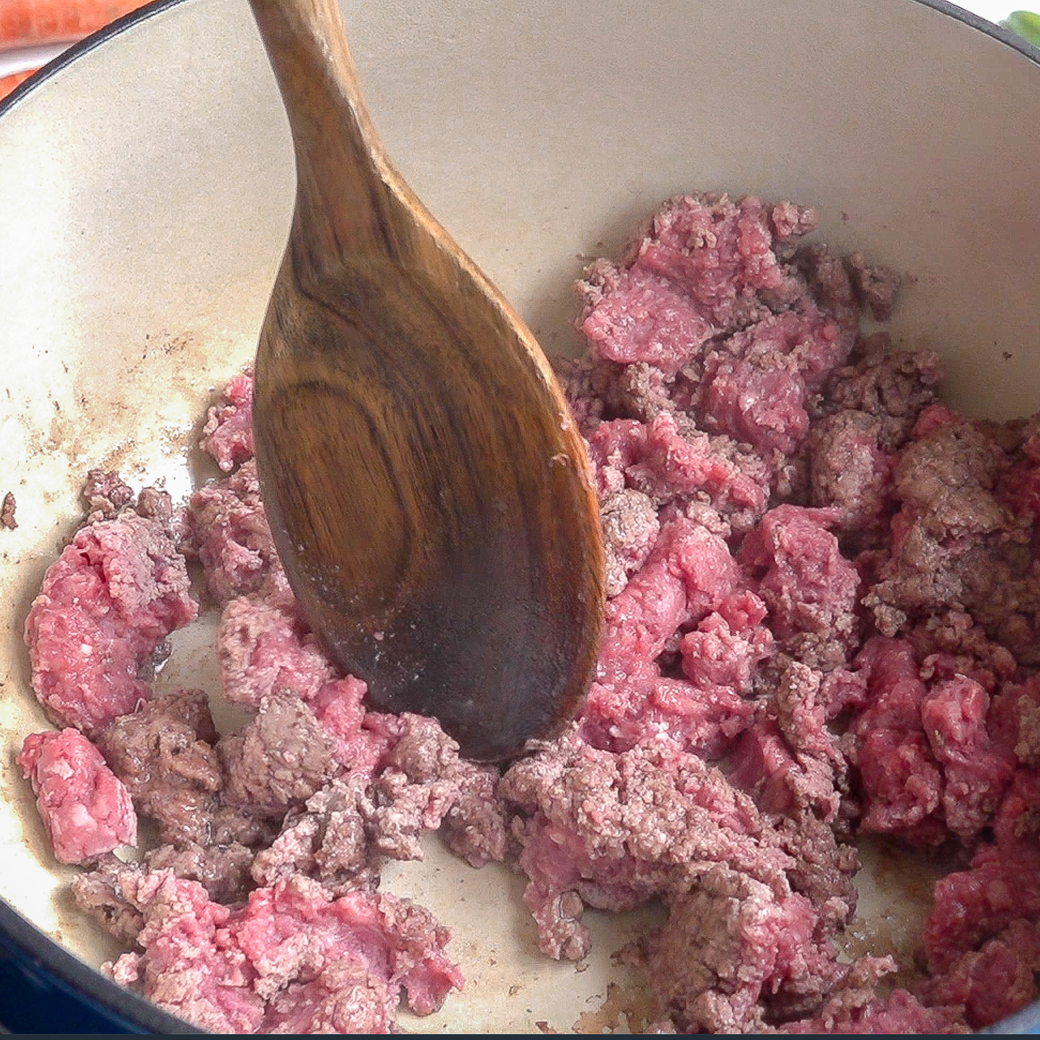 Carne molida cruda en una olla grande, se comienza a cocinar con una cuchara de madera en el centro