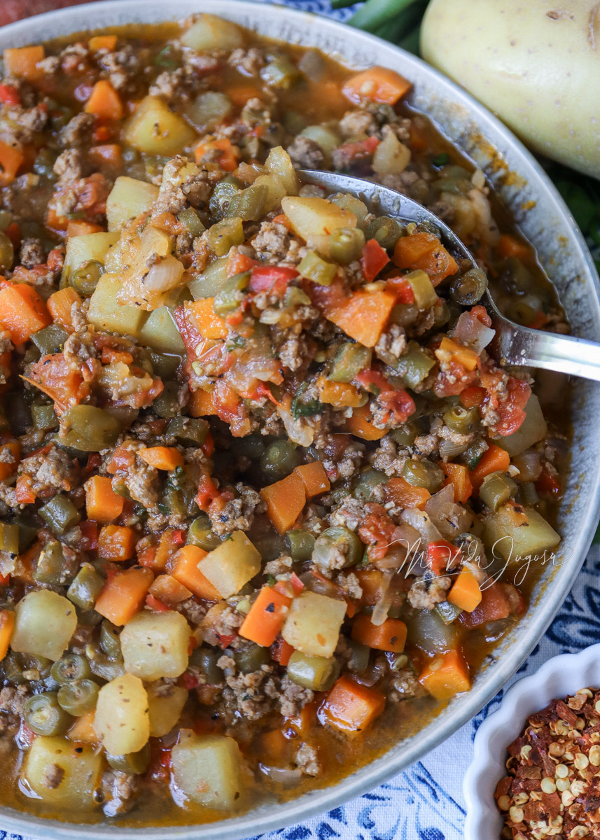 Picadillo de vegetales con carne sobre un plato redondo, rodeado de papas y chile picante