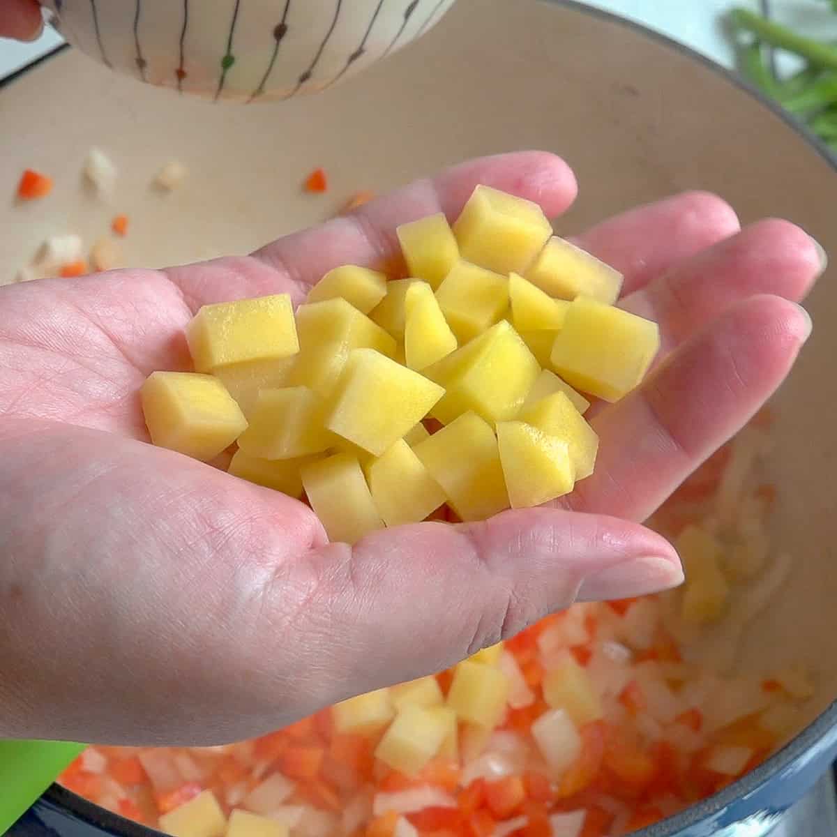 Mano derecha sosteniendo papa cortada en cubos de un mismo tamaño