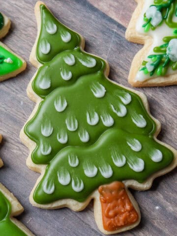 Galleta de mantequilla en forma de árbol de navidad decorada con glaseado real de color verde con copos de nieve color blanco