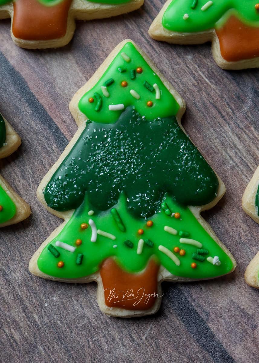 Galleta de mantequilla en forma de arbol navideño decorada con dos tonos diferentes de verde y chispas comestibles