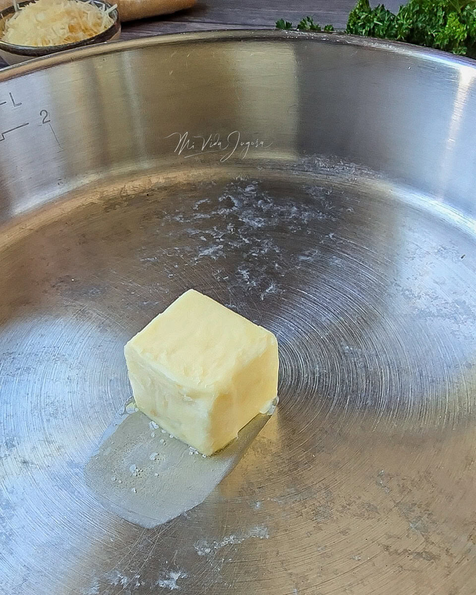 Un sarten de aluminio que contiene un cuadro de mantequilla que comienza a derretir con el calor de la estufa