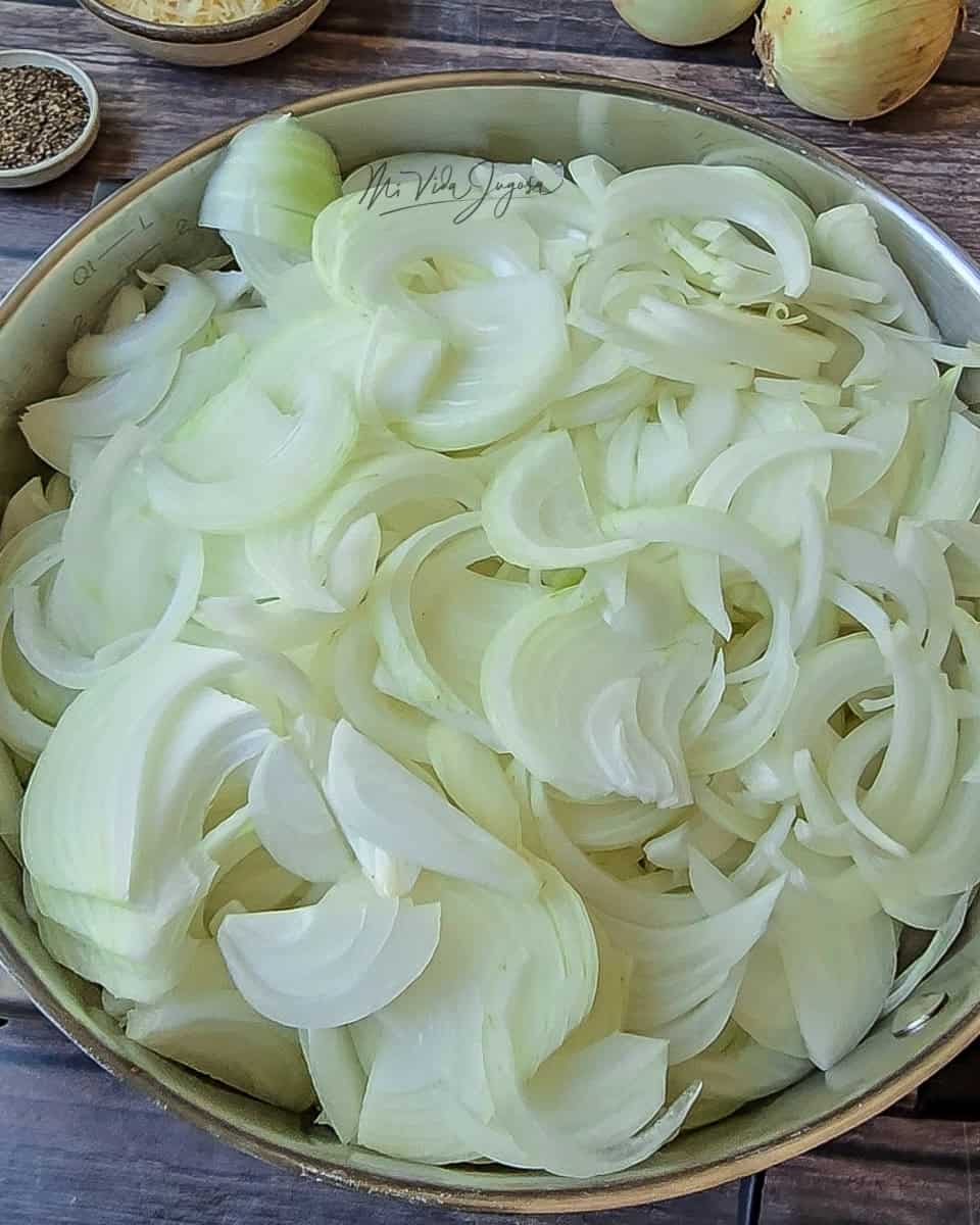 Un sarten extendido que contiene todas las cebollas cortadas en rodajas, las cebollas estan crudas