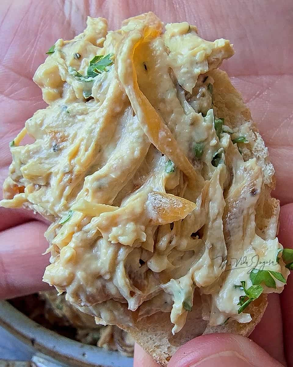 Dip de cebolla caramelizada sobre un pedacito de pan blanco, se observa el detalle de la cebolla caramelizada mezclada con el queso crema y demas ingredientes
