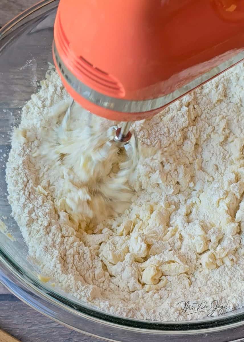 Se muestra la mezcla de mantequilla con harina, sobre un tazon de vidrio y una batidora de mano color coral.