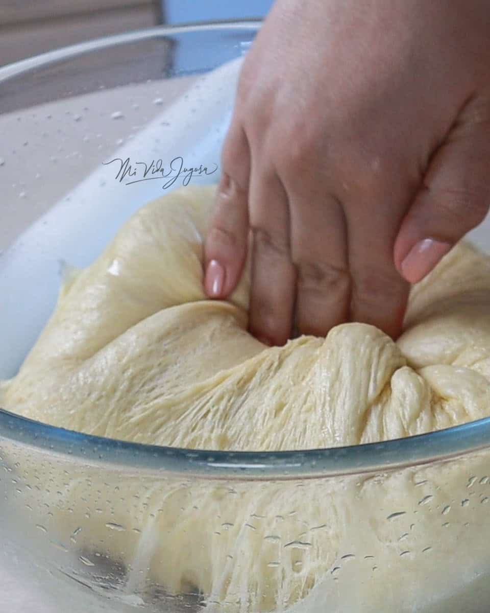 Tazon con una masa leudada y una mano desinflando la masa
