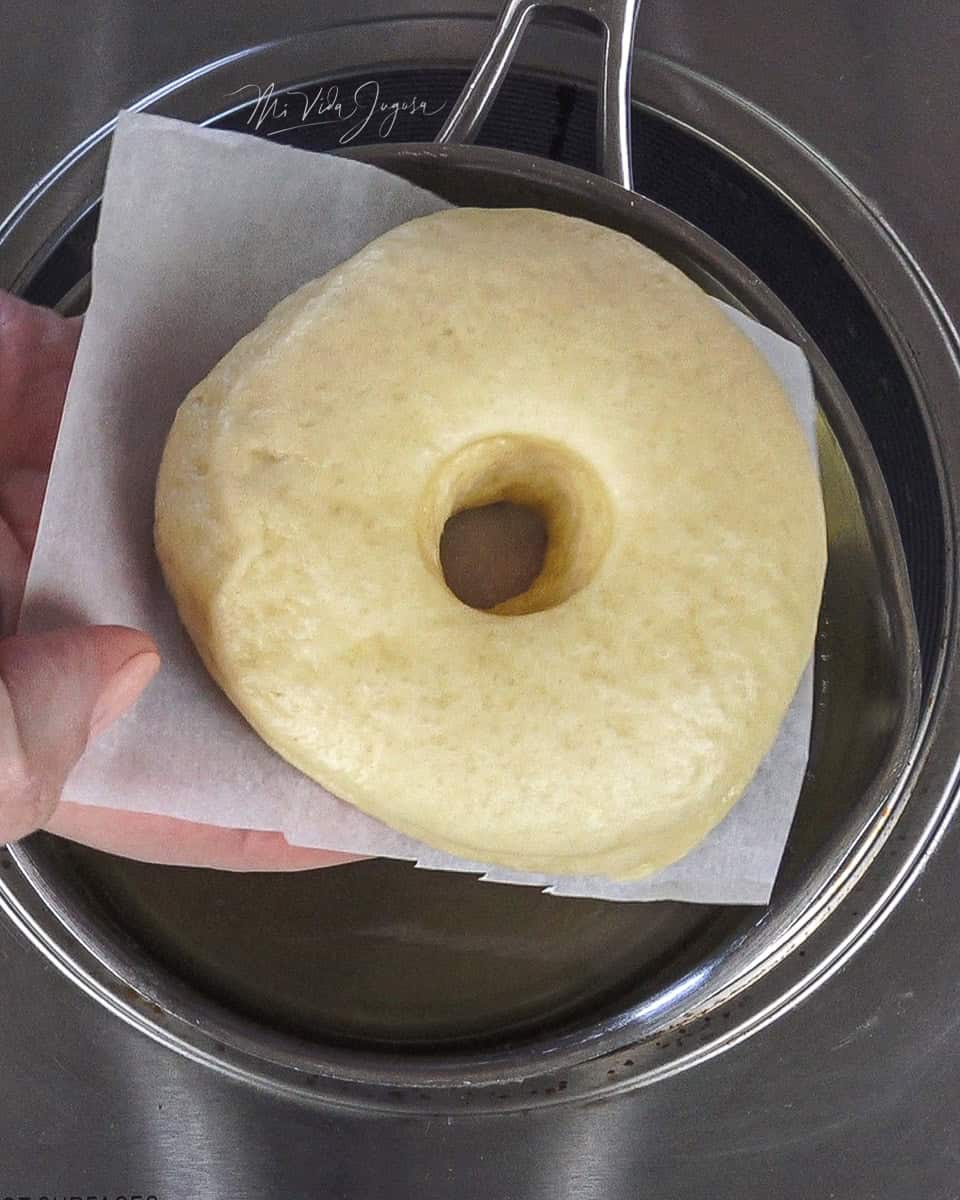Una olla pequeña llena de aceite, y una dona colocada en un pedazo de papel encerado recortado de forma cuadrada