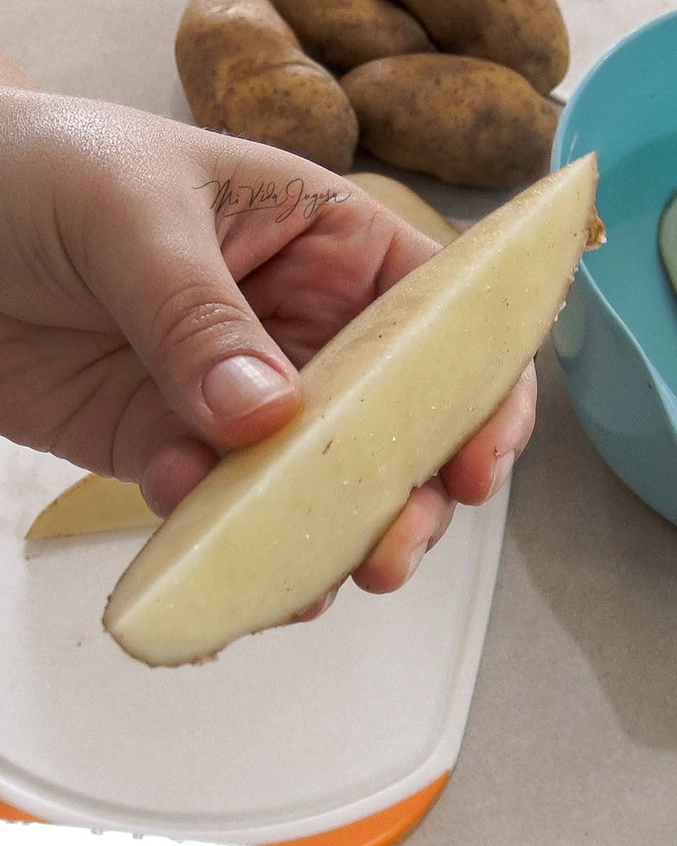 Mano sosteniendo un gajo de papa para mostrar el corte y tamaño