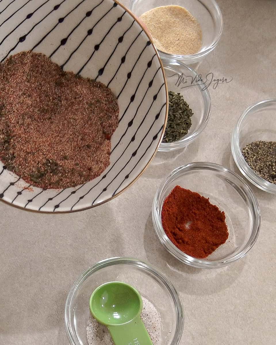 5 recipientes pequeños con los siguientes ingredientes: Ajo en polvo, oregano,paprika, pimienta y sal. En un bowl los ingredientes mezclados.