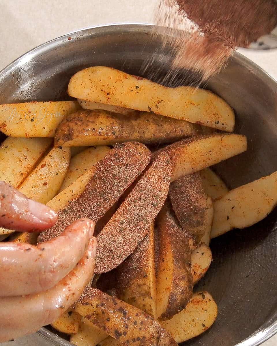 Tazon con papas cortadas en forma de gajo, y se muestra como se le espolvorean los condimentos encima a las papas.
