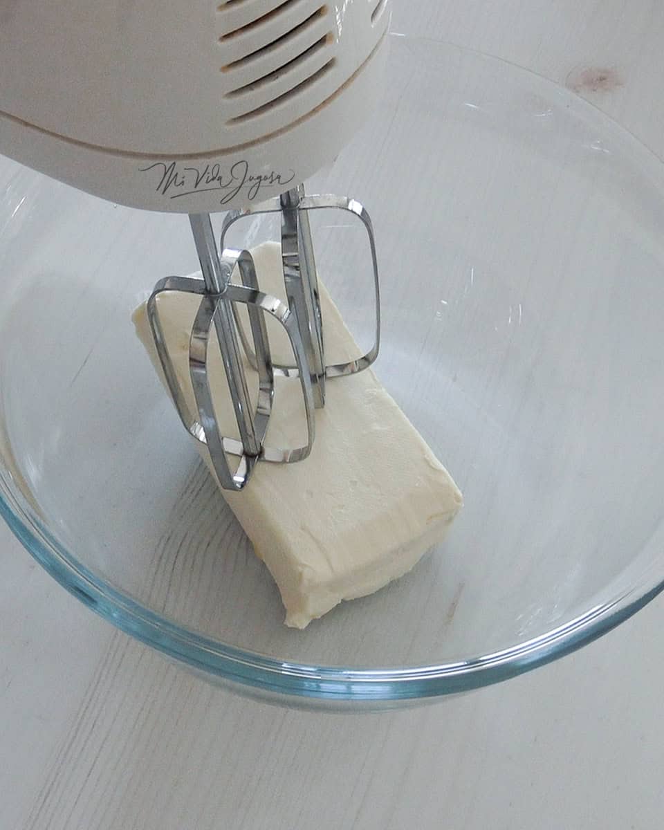 Bloque de queso crema en un tazón y una batidora de mano con sus aspas directamente sobre el queso