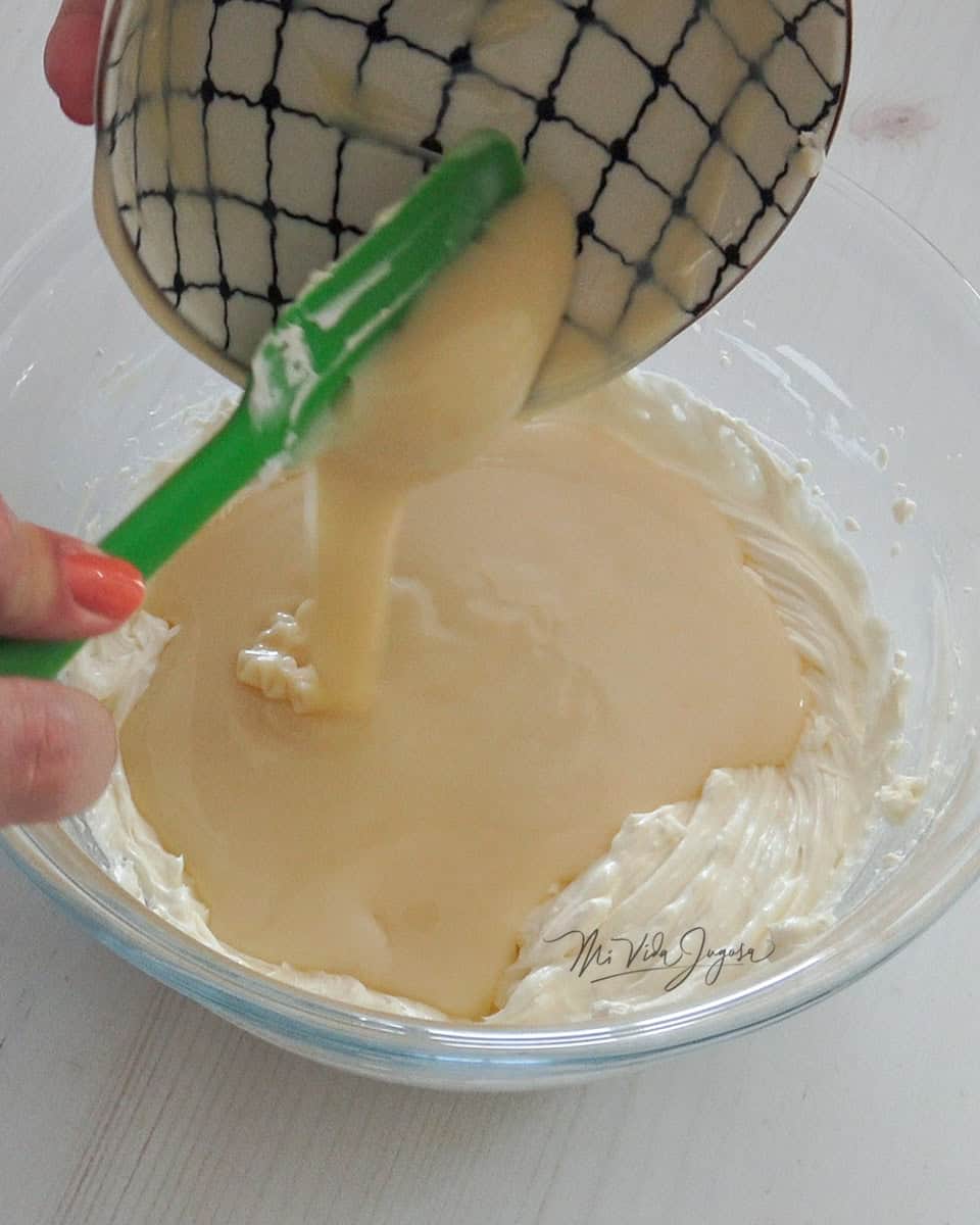 Se vierte leche condensada sobre un tazón con la mezcla de queso crema