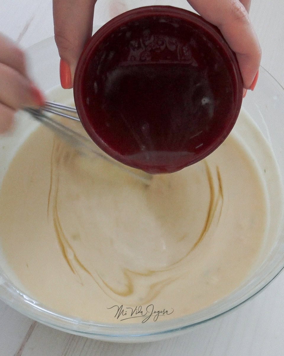 En un tazón transparente que contiene la mezcla de queso crema, leche condensada y las ralladuras de limón y naranja se le agrega la grenetina derretida