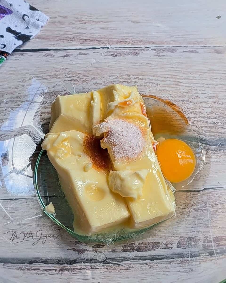 Tazon conteniendo dos barras de mantequilla, un huevo, sal, extracti de vainilla y  rayadura de naranja