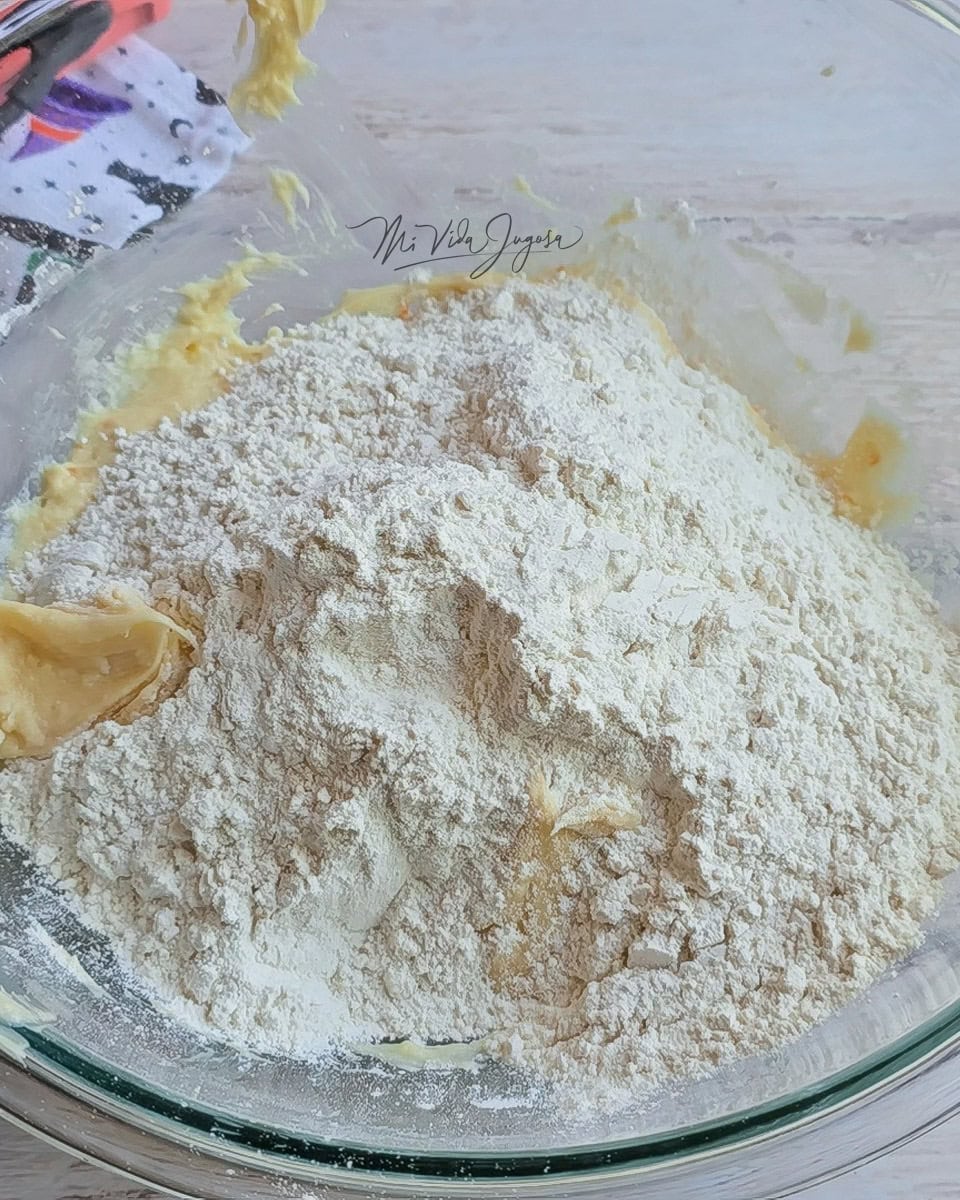 Tazon de vidrio donde se visualiza que se esta agregando la harina a la mezla de ingredientes humedos.