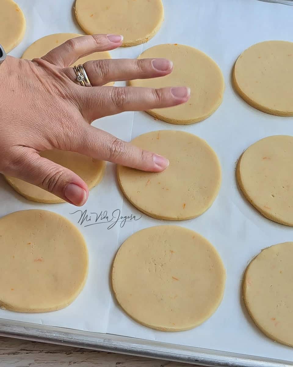 Una bandeja de aluminio con un pliego de papel encerado, conteniendo las galletas cortadas de forma circular, listas para ser horneadas