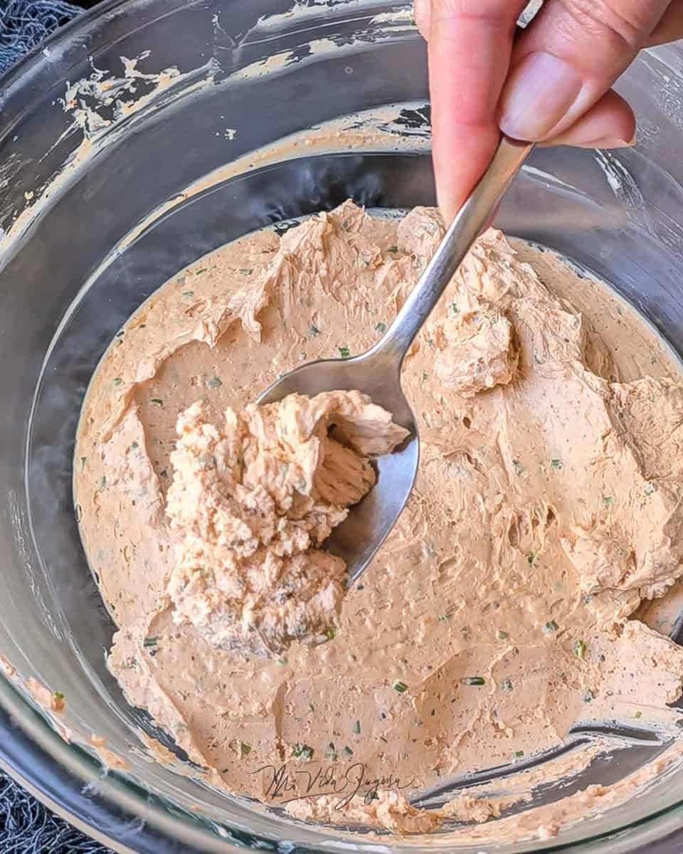 Un bowl de vidrio conteniendo la mezcla en segundo plano, y encima exhibiendo una cuchara con un poco de la mezcla