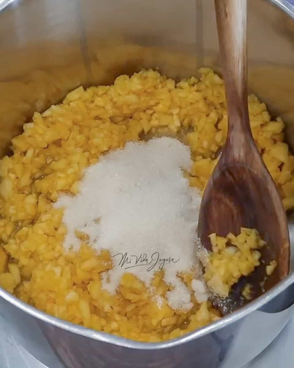 Un bowl de aluminio conteniendo piña picada en finos cuadritos y la azucar blanca. 