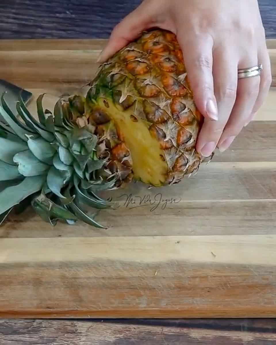 Fotografia donde se muestra una  tabla de madera en la que se esta cortando la corona de una piña.