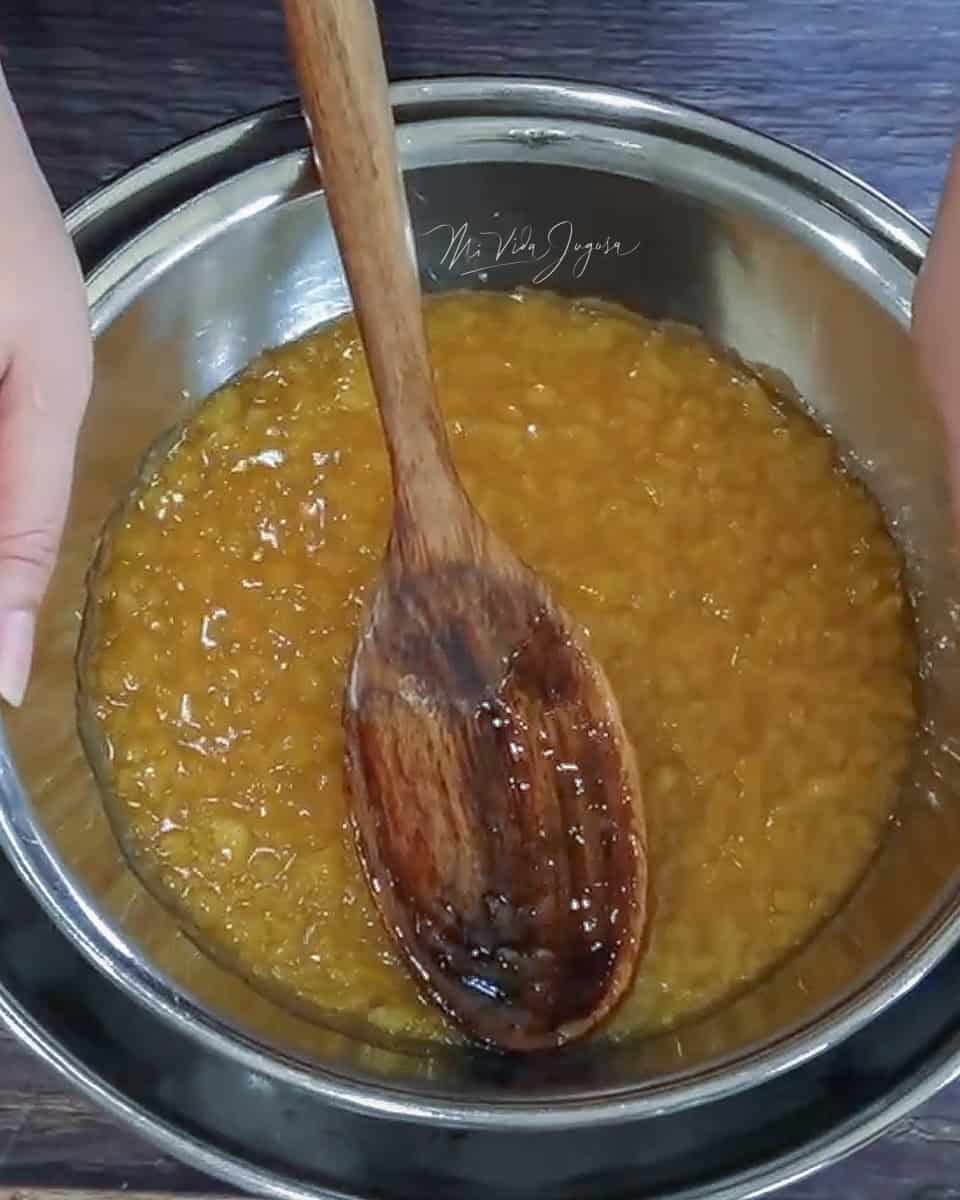 Se observa una olla con la mermelada de piña lista sumergida en un recipiente lleno de hielo, y una cuchara de madera.