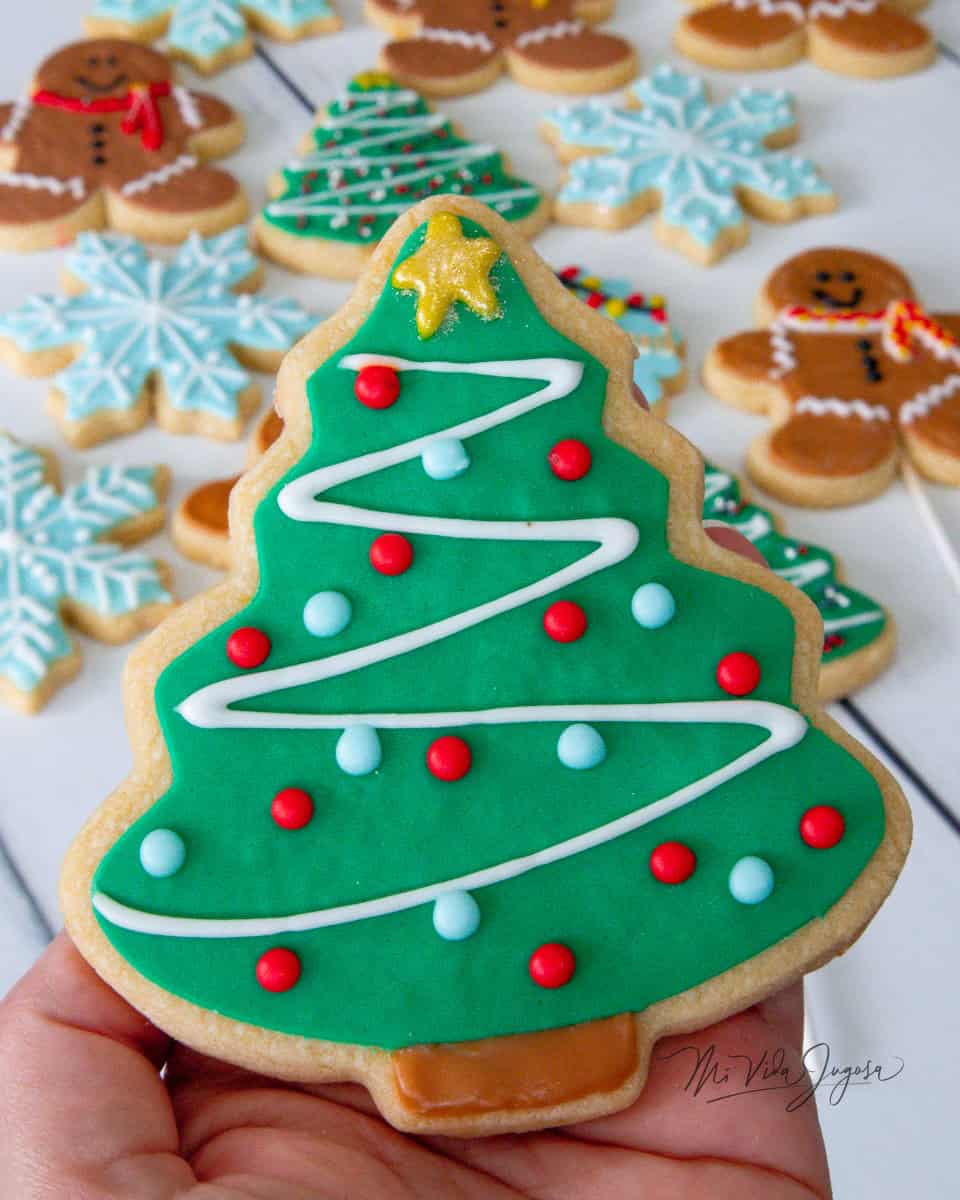Galleta de forma de árbol de navidad decorada con glaseado verde, una estrella y algunas bolitas de color 
