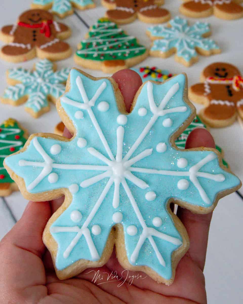 Una galleta de forma de copo de nieve decorada de color celeste y las lineas blancas que semejan la forma de copo
