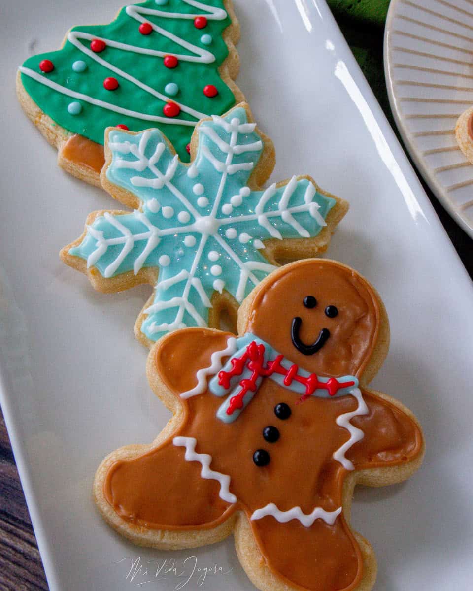En un plato alargado de color blanco se exhiben galletas en forma de muñeco de gengibre, copo de nieve y árbol de navidad