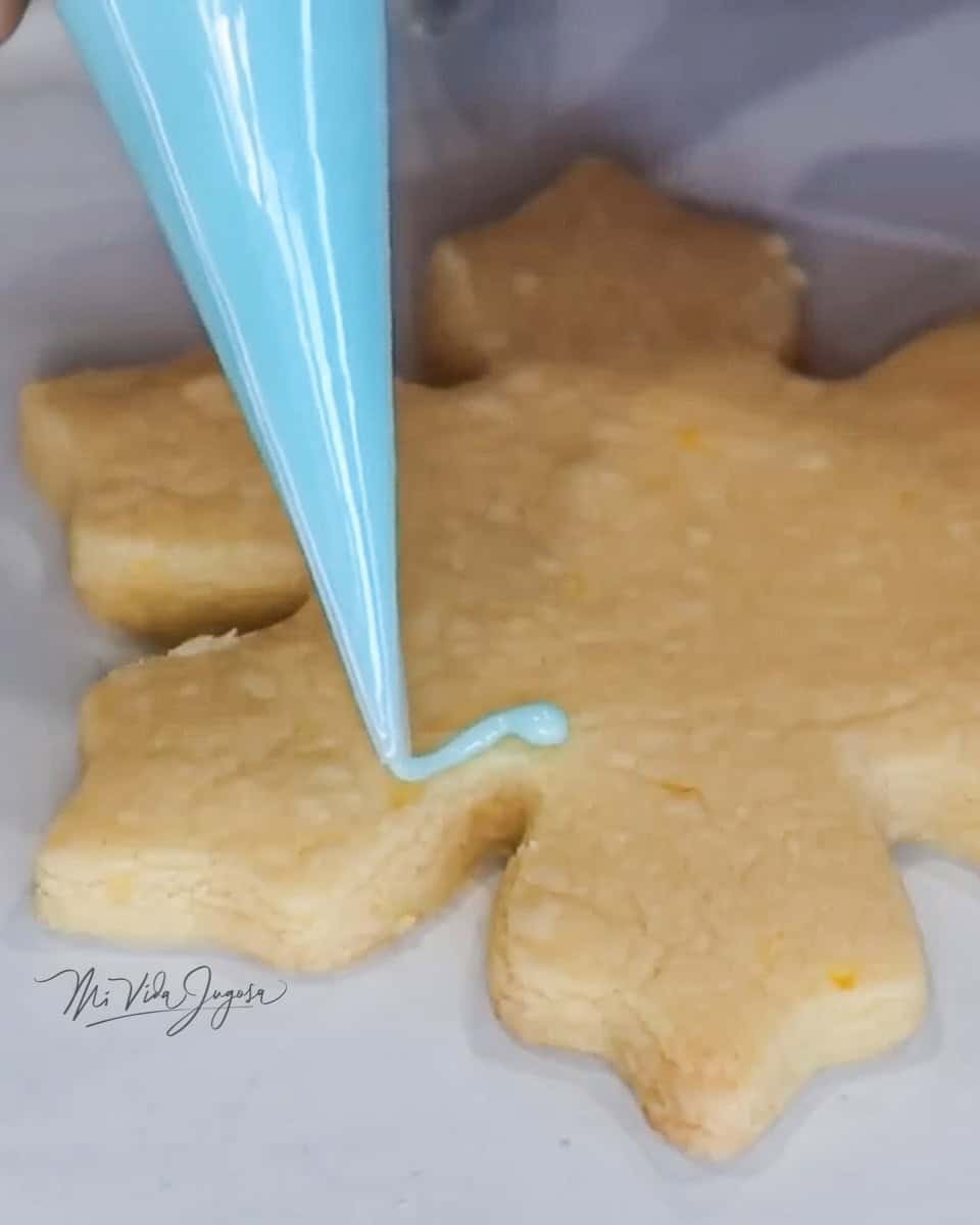 Una galleta de forma de copo de nieve, donde se esta empezando a aplicar el glaseado decorativo de color celeste, en sus orillas
