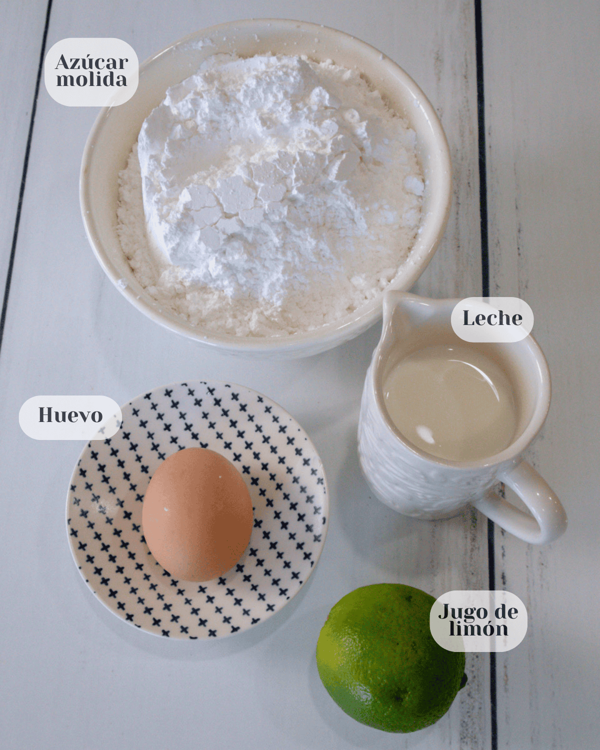 Una taza conteniendo el azúcar molida, un plato con un huevo entero, una contenedor con leche y un limon.