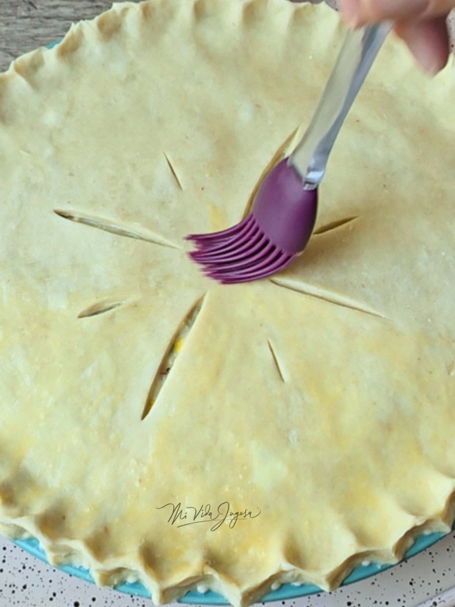 Una brocha para cocina untandole la mezcla de huevo a la masa que recubre el pie.