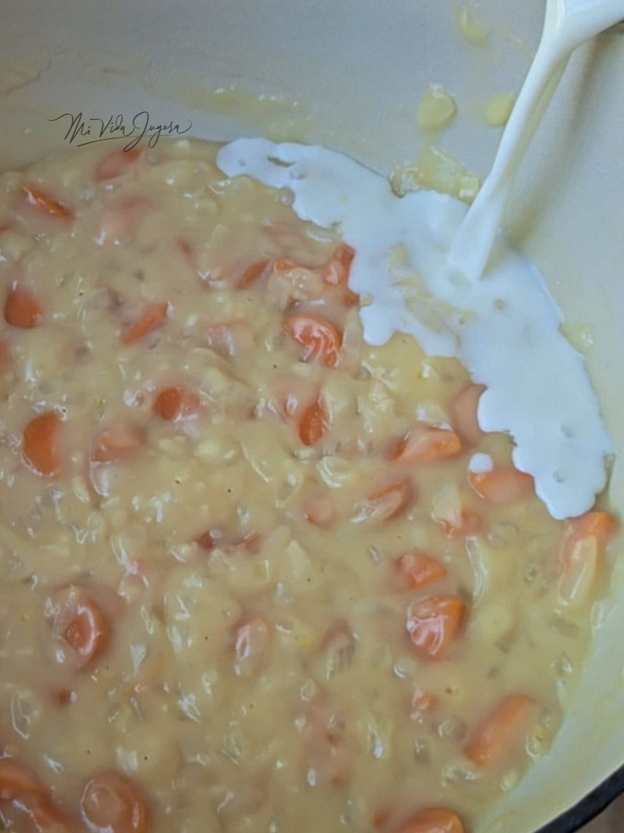 Picadillo de zanahoria con cebolla en una salsa viscosa, un chorrito de leche cayendo dentro de la olla