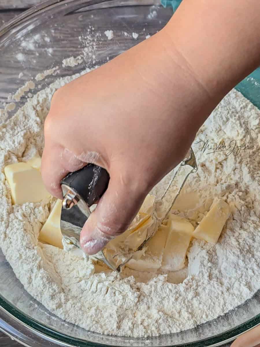 na mano trabajando la mantequilla con un cortador, incorporándola poco a poco a la mezcla de harina.