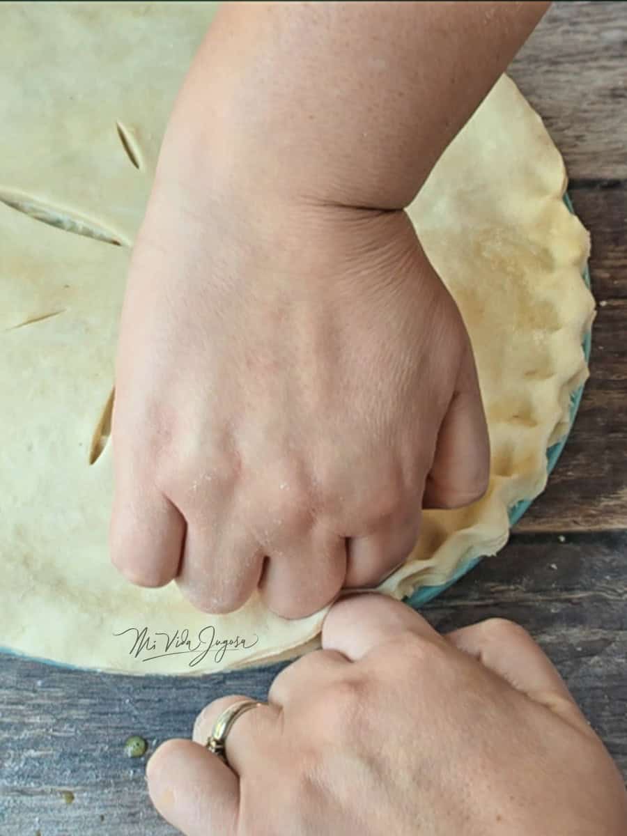 Una mano por dentro del molde formando una pequeña “V”, mientras la otra presiona la masa desde afuera para dar forma a los bordes.
