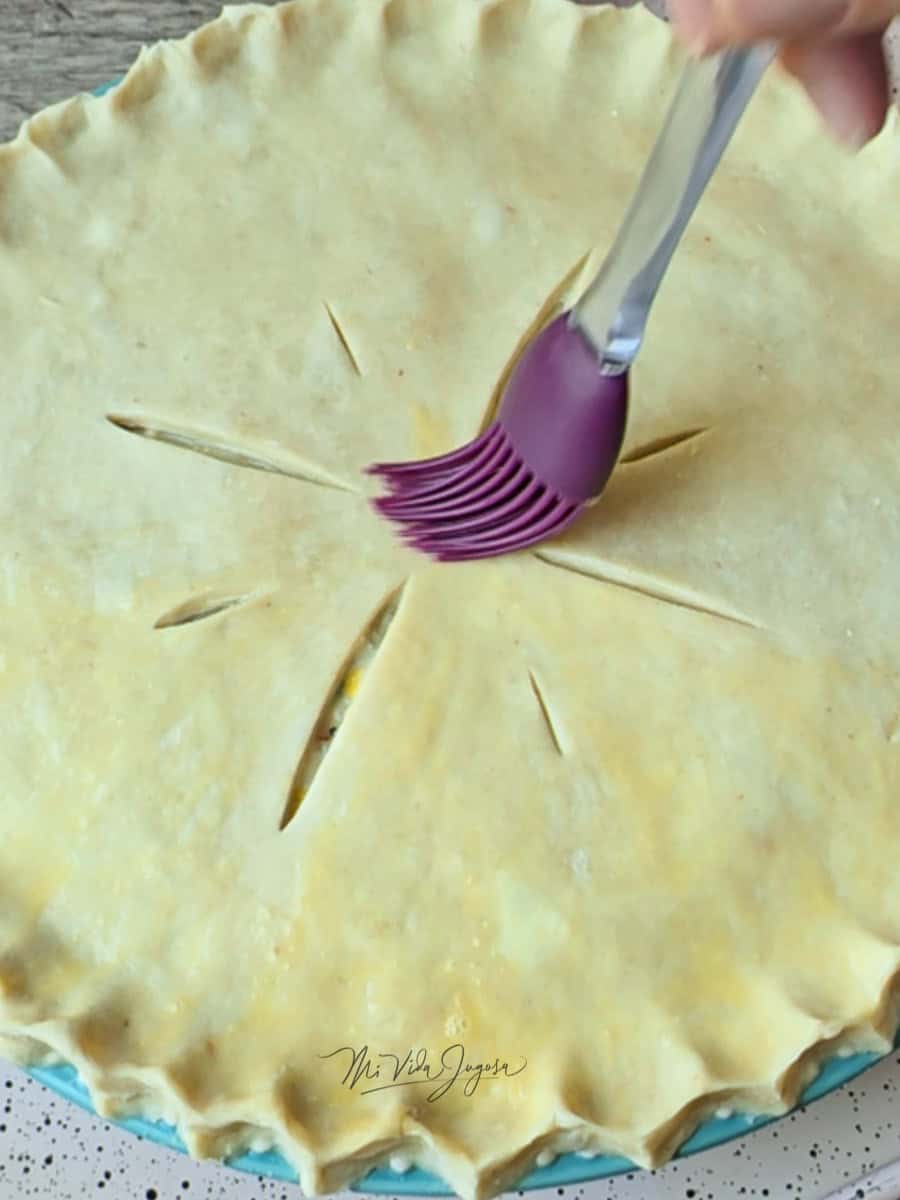 Una brocha de cocina barnizando con huevo batido la tapa superior del pie.