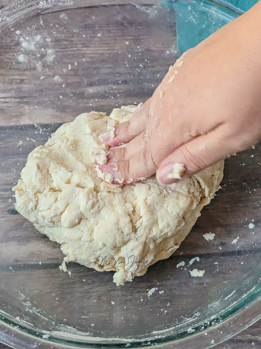 Un tazón con una bola de masa mientras una mano la presiona suavemente.