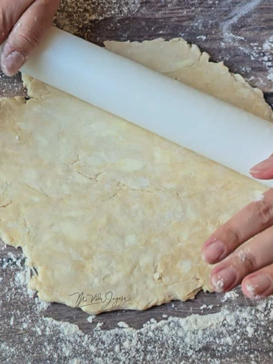 Una masa siendo aplanada con un rodillo por dos manos.