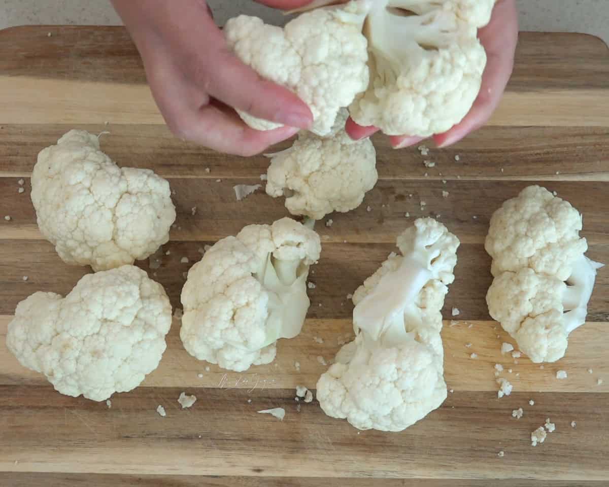 Una tabla de picar con floretes de coliflor, dos manos por encima sosteniendo el resto de la coliflor