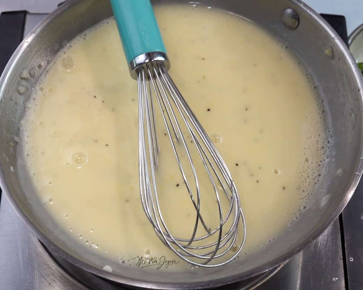 Una cacerola con la salsa en su interior y un batidor de globo colocado dentro.