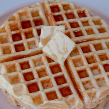Un waffle servido con unos cuadritos de mantequilla y sirope de maple por encima
