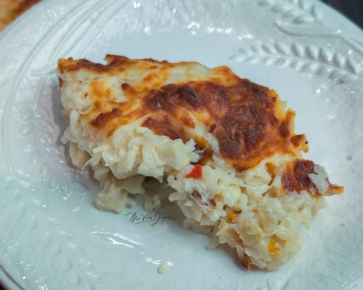 Un plato blanco con arroz cremoso y pedacitos de palmito, cubierto con queso gratinado por encima.