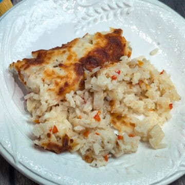 Un plato blanco con arroz cremoso y pedacitos de palmito, cubierto con queso gratinado por encima.