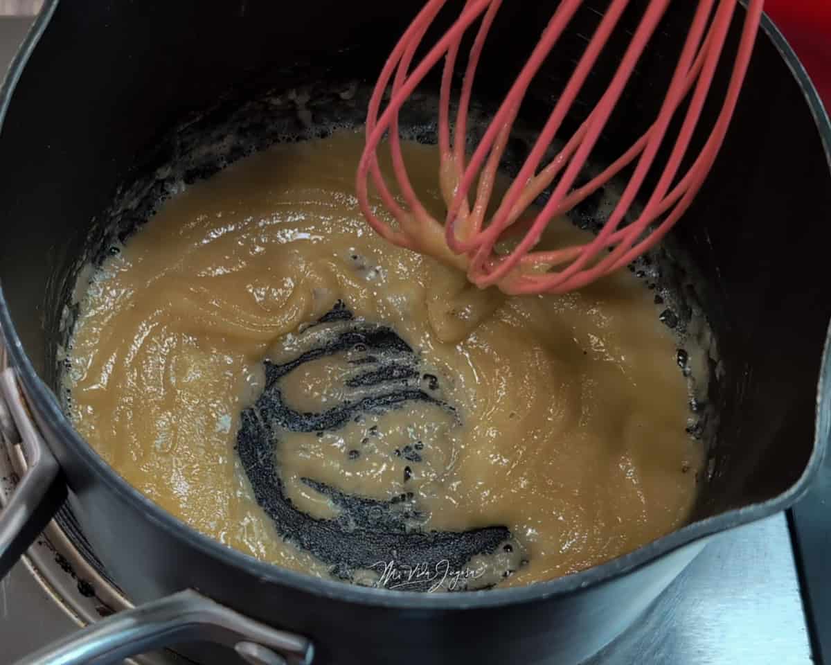 Una olla con una mezcla de mantequilla y harina, siendo revuelta con un batidor de globo.