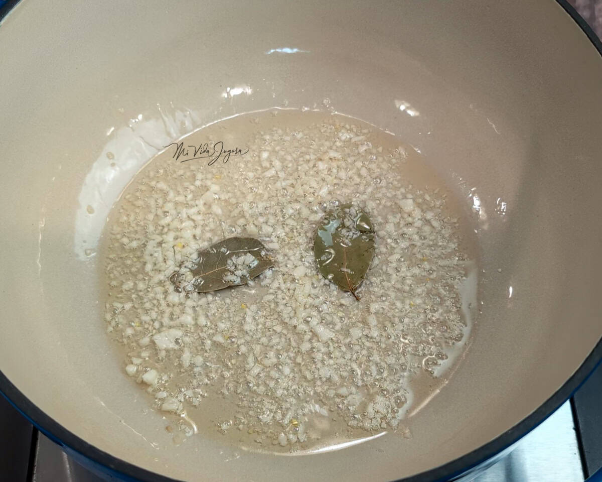 Una olla con pedacitos de ajo bañándose en aceite, junto con unas hojas de laurel.