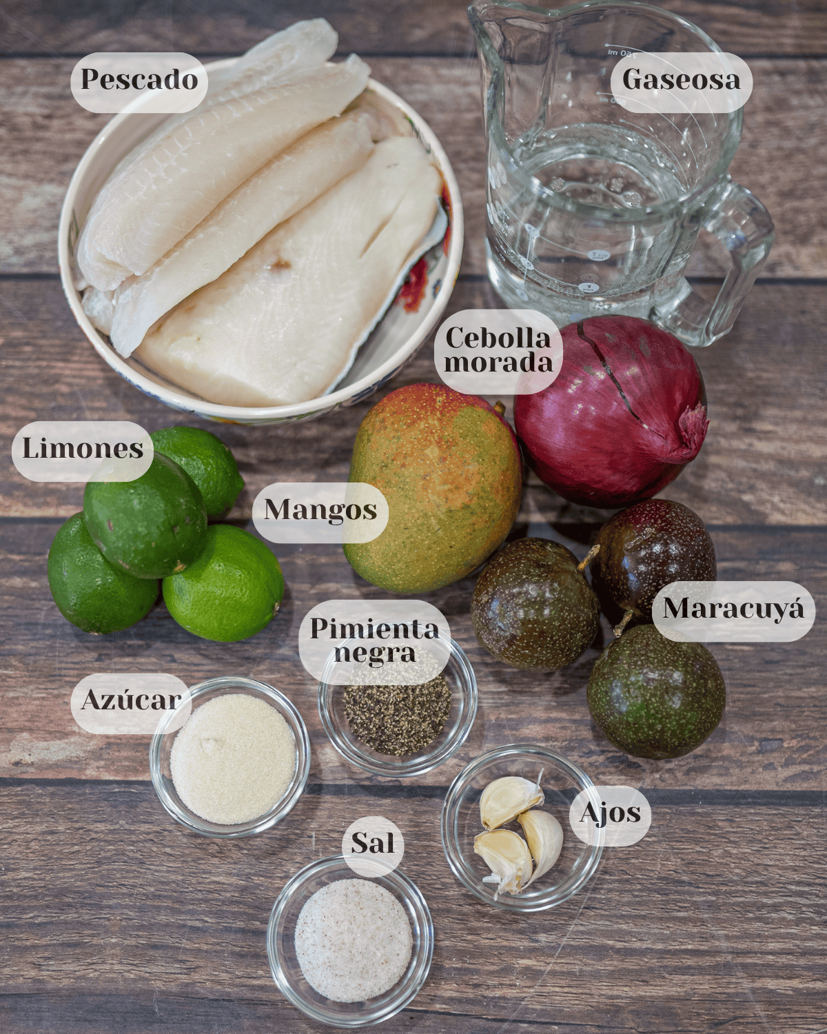 Una foto tomada desde arriba donde se ven los ingredientes: pescado en un pequeño tazón, una taza medidora con Sprite, una cebolla morada, un mango, tres maracuyás, cuatro limones, una tacita con pimienta negra, tres dientes de ajo, azúcar y sal.