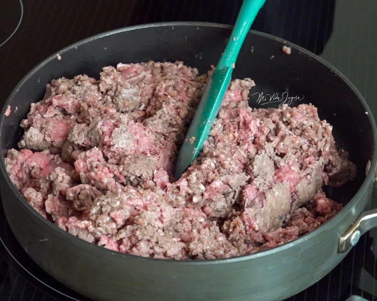 Un sartén con carne molida cocinándose, mientras una espátula la revuelve y la separa en pedacitos.