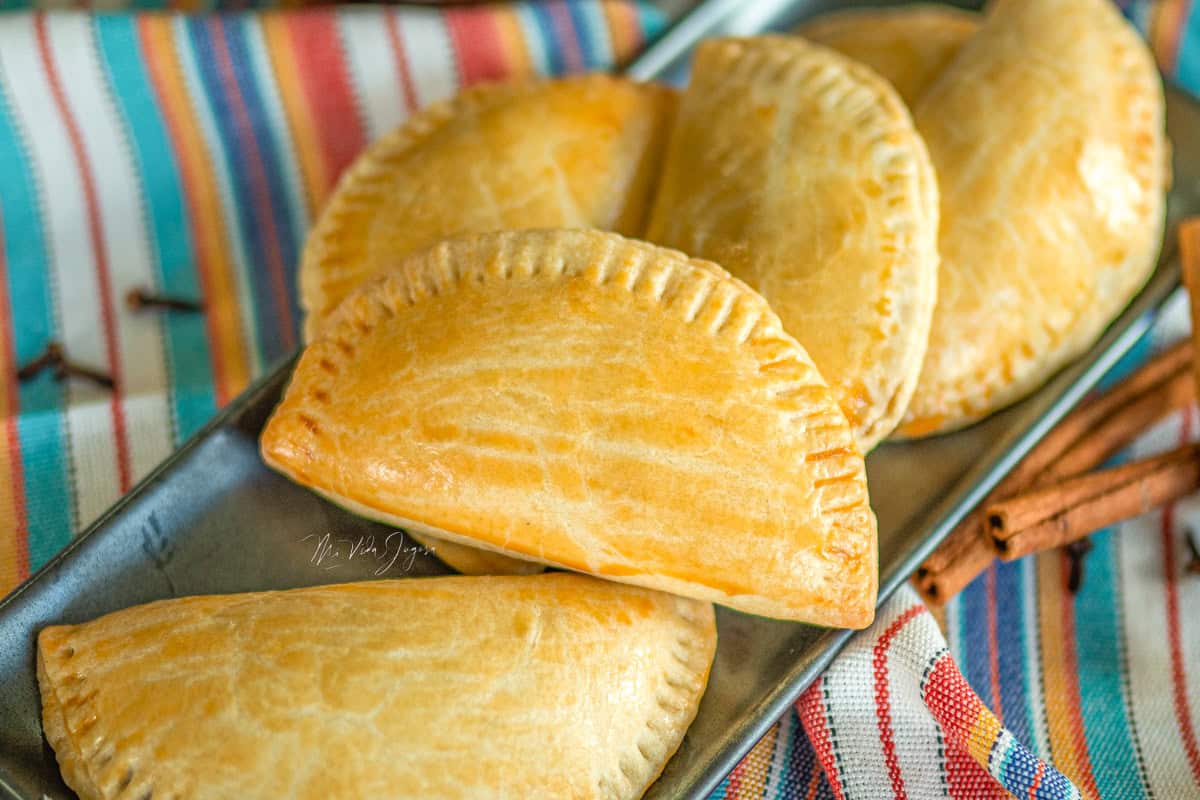 Un platon con empanadas de chiverre encima de un mantel decorativo, con astillas de canela y clavos de olor decorando.