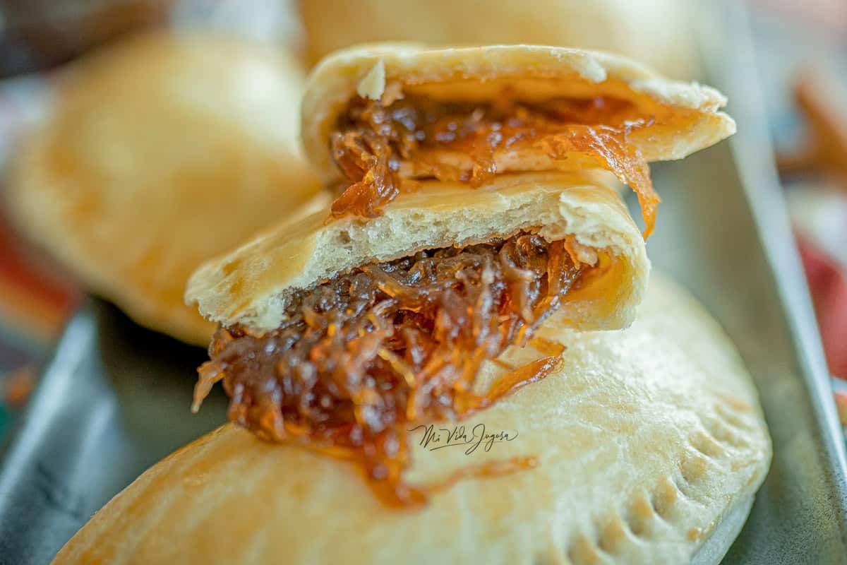 Un plato con varias empanadas de chiverre cocinadas, mientras una por encima se encuentra partida a la mitas y se muestra el relleno de chiverre.